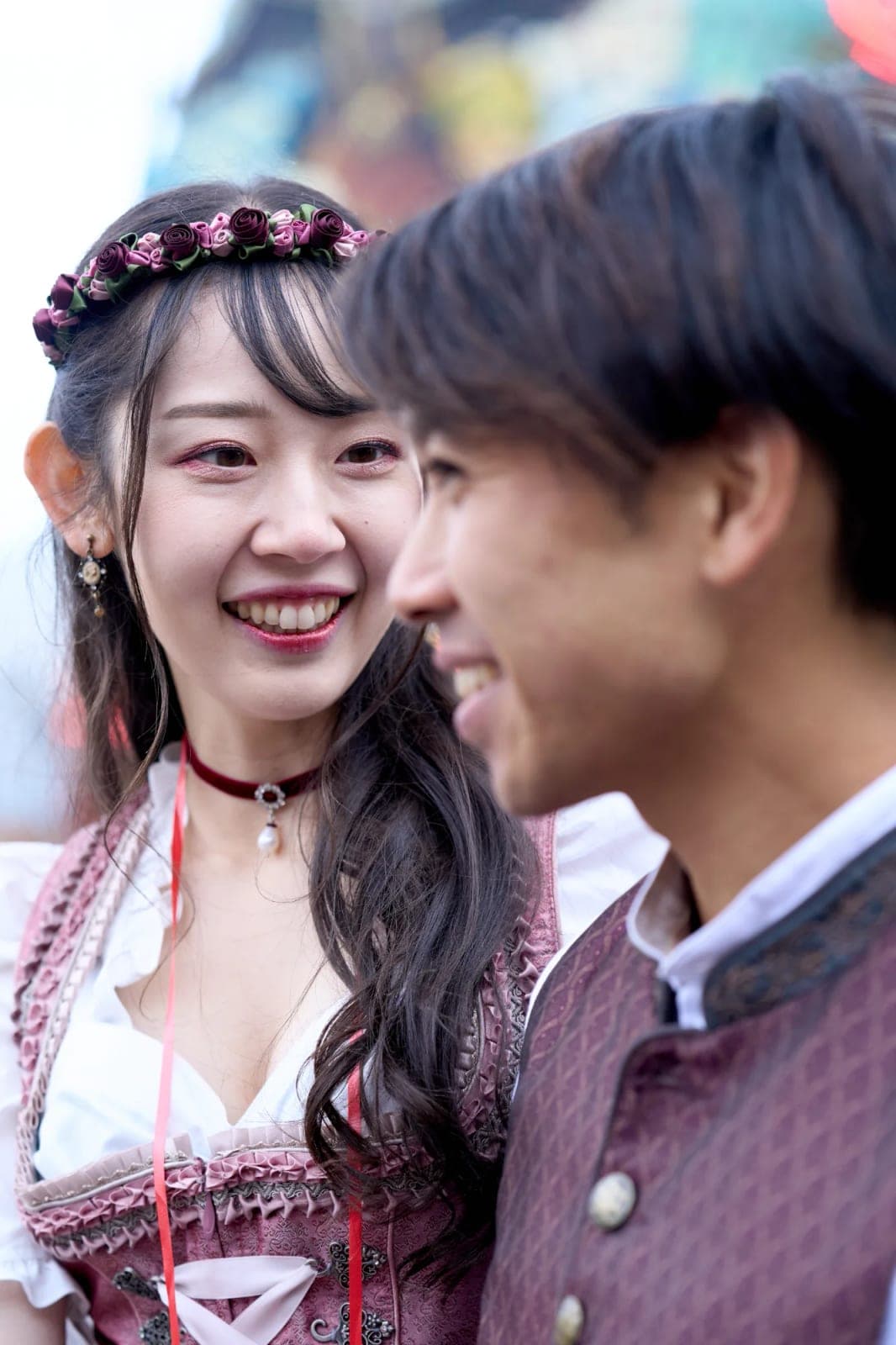 Engaged couple in traditional Tracht laughing together among colourful rides during an engagement photoshoot at Oktoberfest in Munich